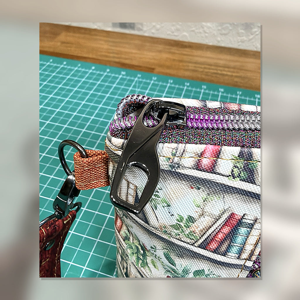 Close-up of top zipper hardware and bookshelf fabric on Book Nook Crossbody Bag