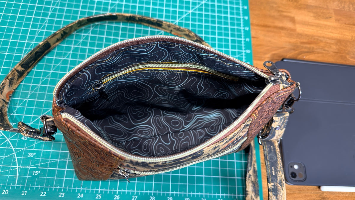 Overland Crossbody bag opened to show blue topographic contour-line fabric lining and interior zipper pocket