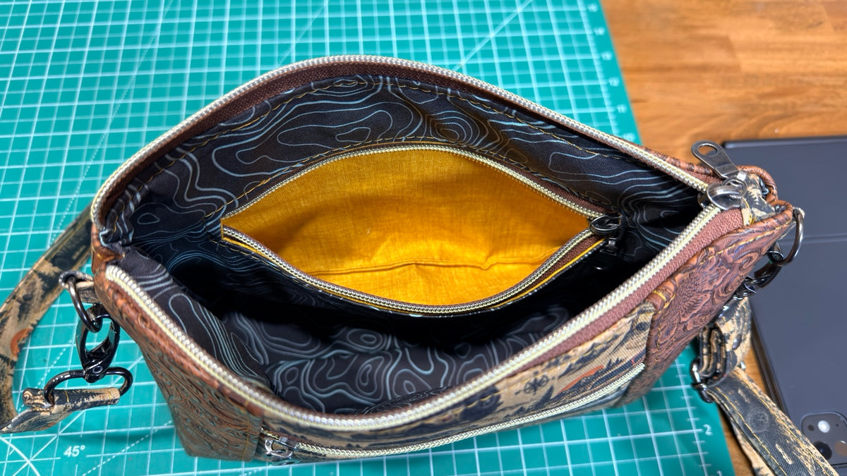 Close-up of Overland Crossbody blue topo interior lining with open yellow-lined zipper pocket